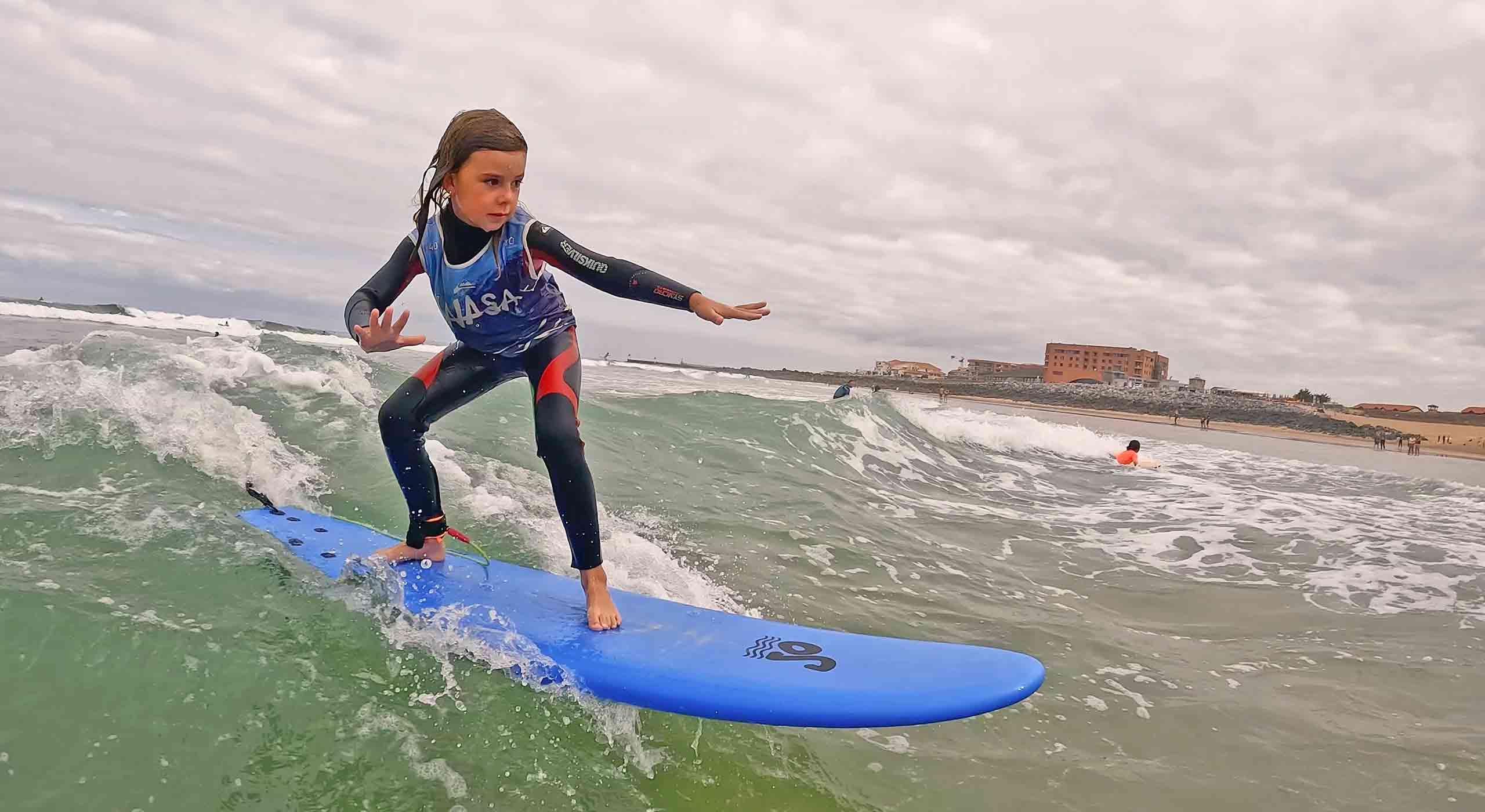 fillette sur planche en mousse bleu dans la vague en cours de surf enfant à capbreton