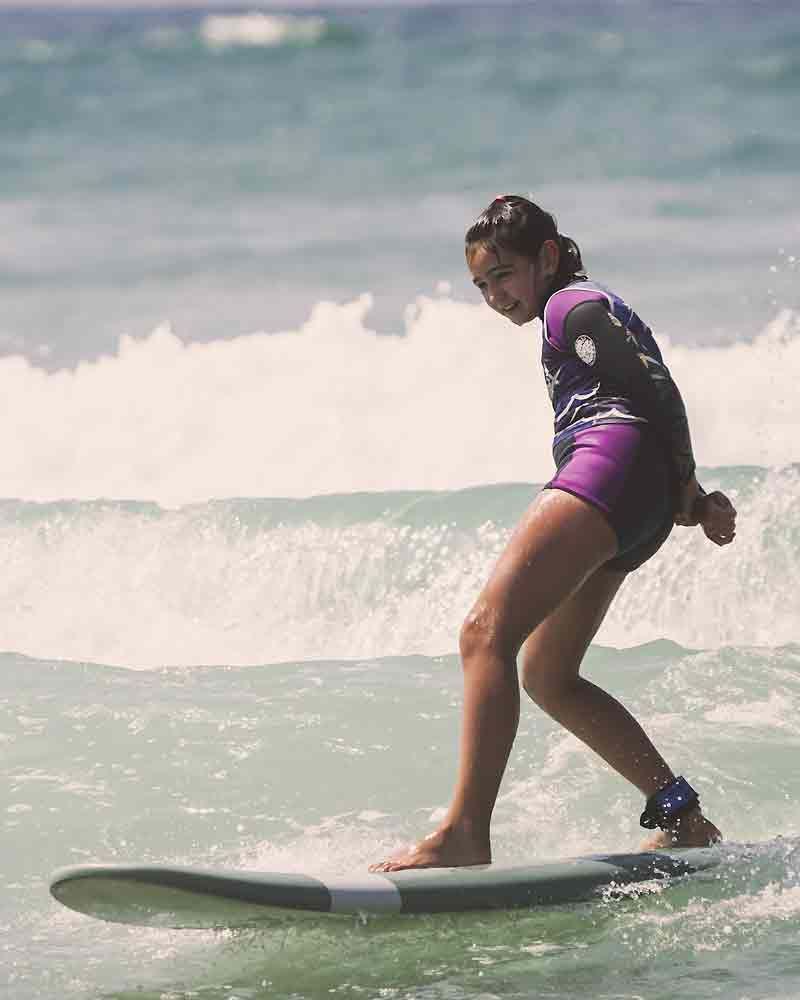 surfeuse enfant sur une petit vague l'été surfant les mains dans le dos